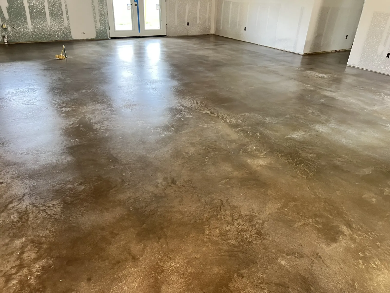Open floor in polished and sealed concrete, mottled tan and grey, walls still unfinished